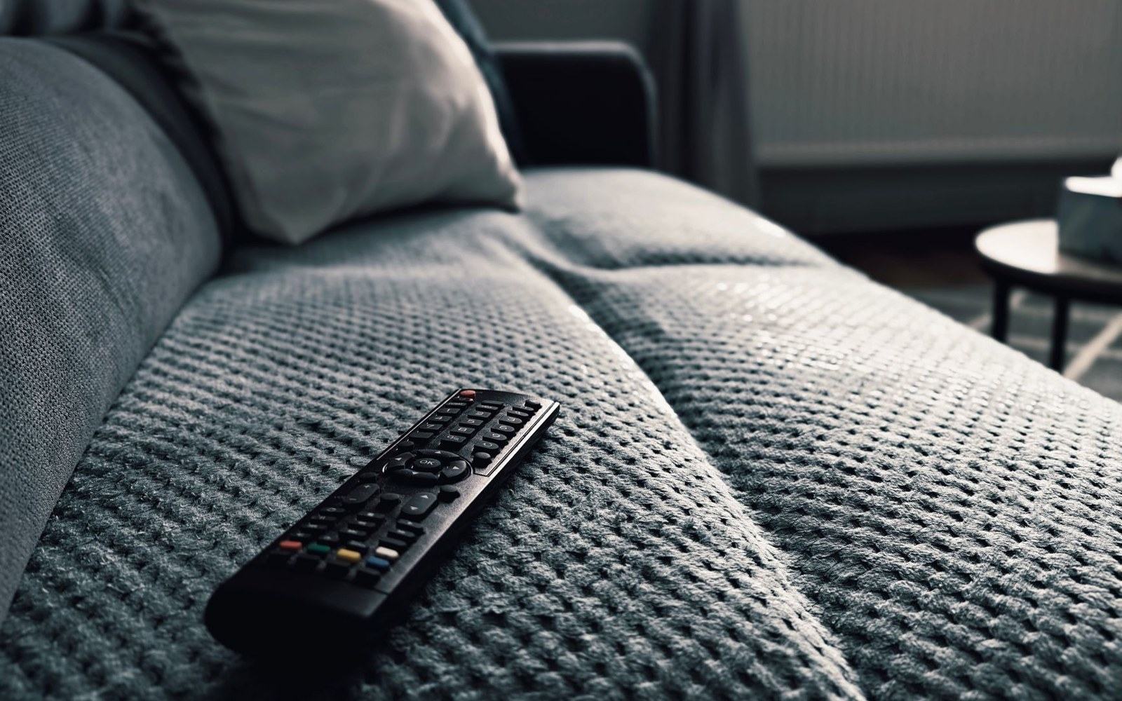 A tv remote control resting on the textured cushion of a grey sofa