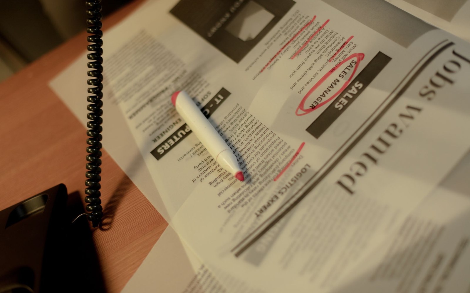 A red marker circles job listings on a newspaper's classified jobs wanted section