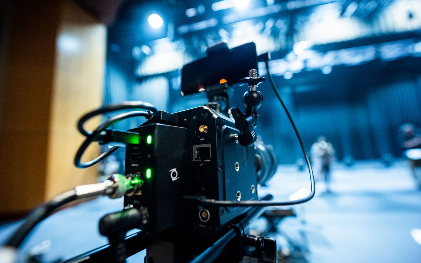A film camera rig with cables and glowing indicator lights on a dim studio set
