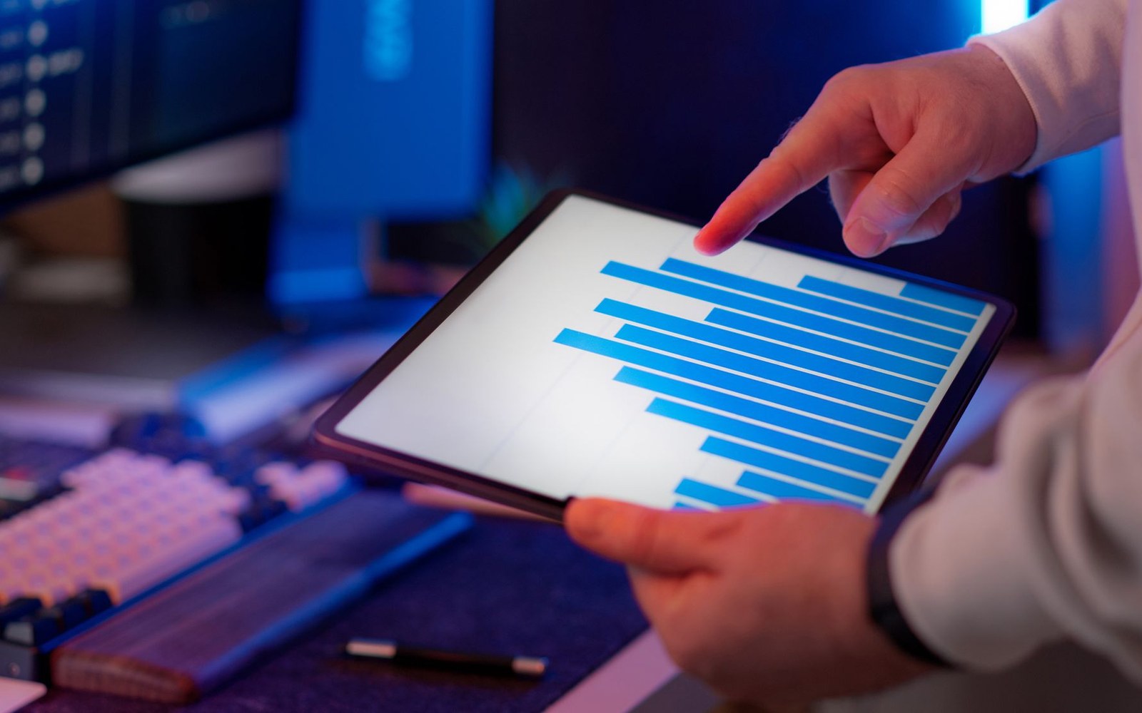 A hand points to a horizontal bar chart displayed on a tablet held over a desk