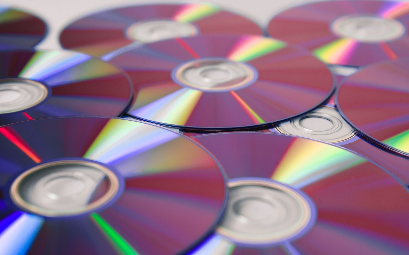 Overlapping CDs or DVDs reflect rainbow light patterns across their surfaces