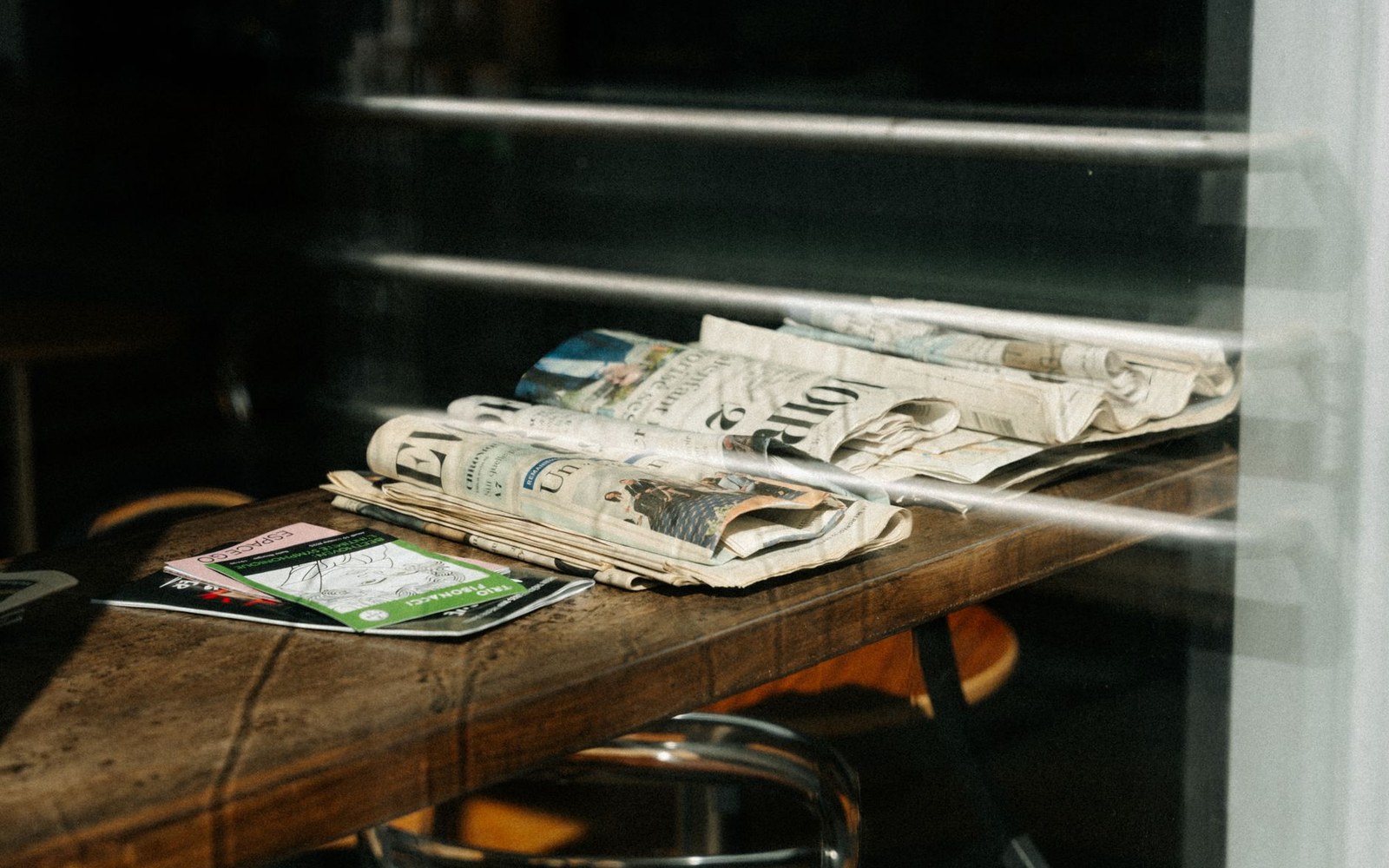 Folded newspapers stacked on a wooden counter beside a green flyer
