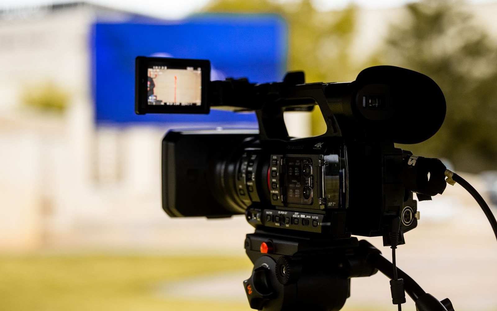 A video camera on a tripod outdoors with its flip-out screen displaying footage