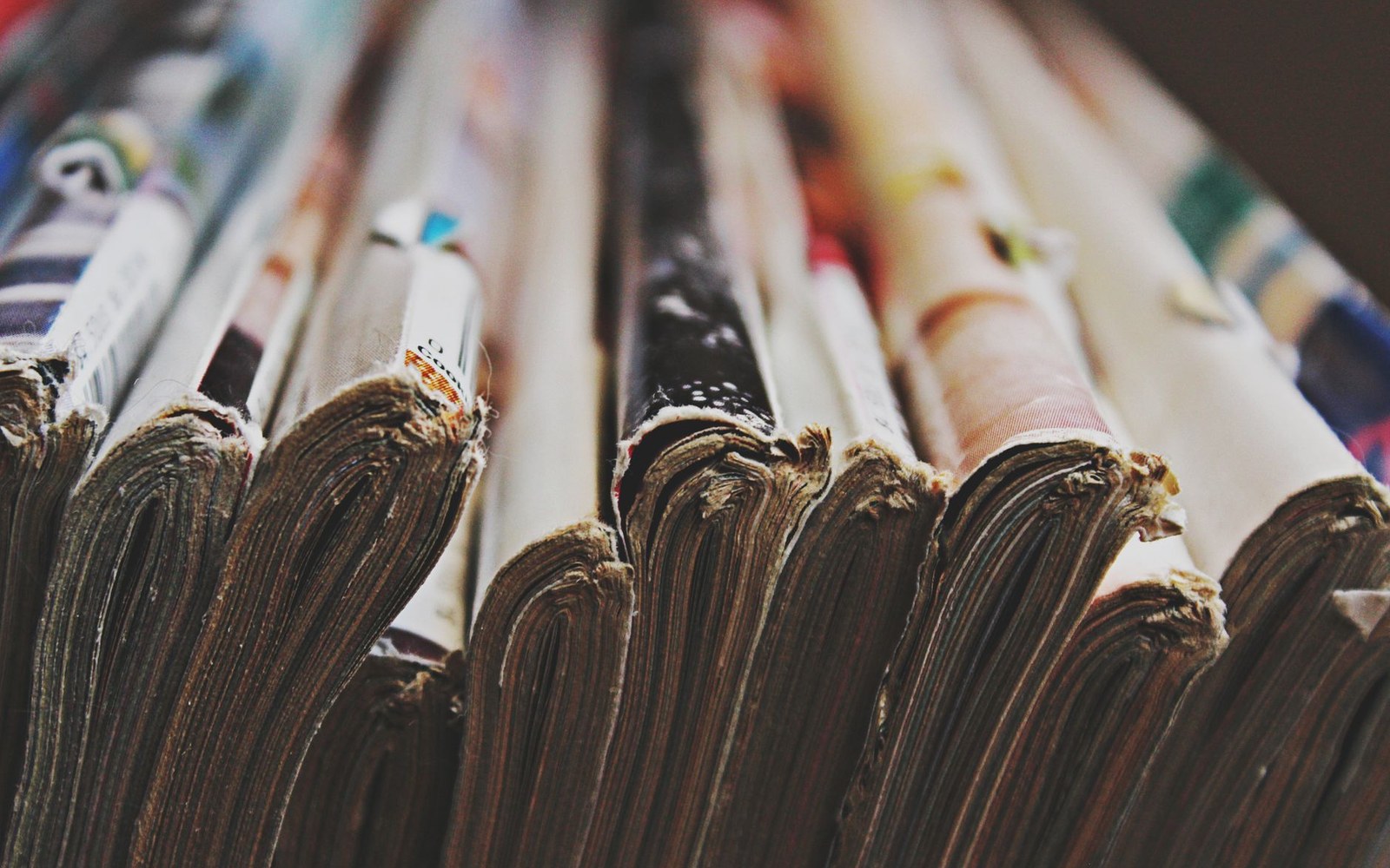 Close-up of folded newspapers stacked side by side, spines facing forward