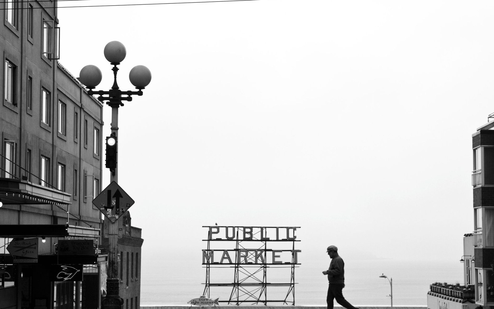 A pedestrian walks past the Public Market sign near a street lamp overlooking the water