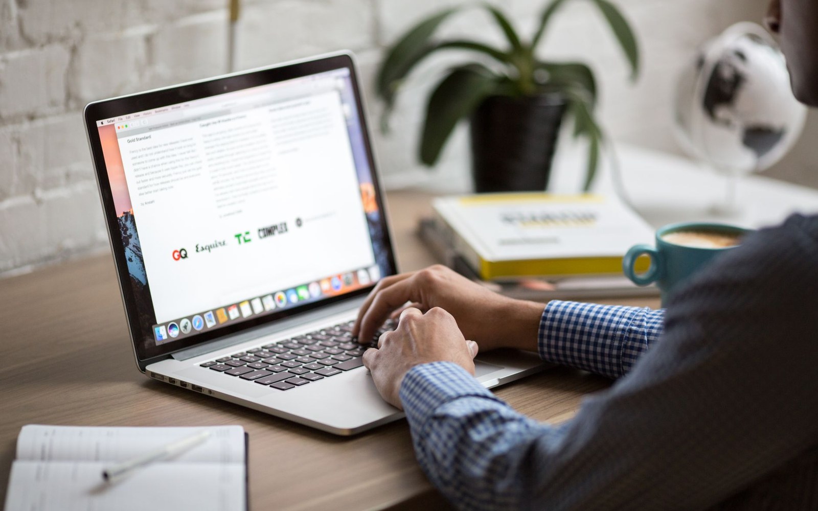 Person typing on a laptop displaying a document at a wooden desk