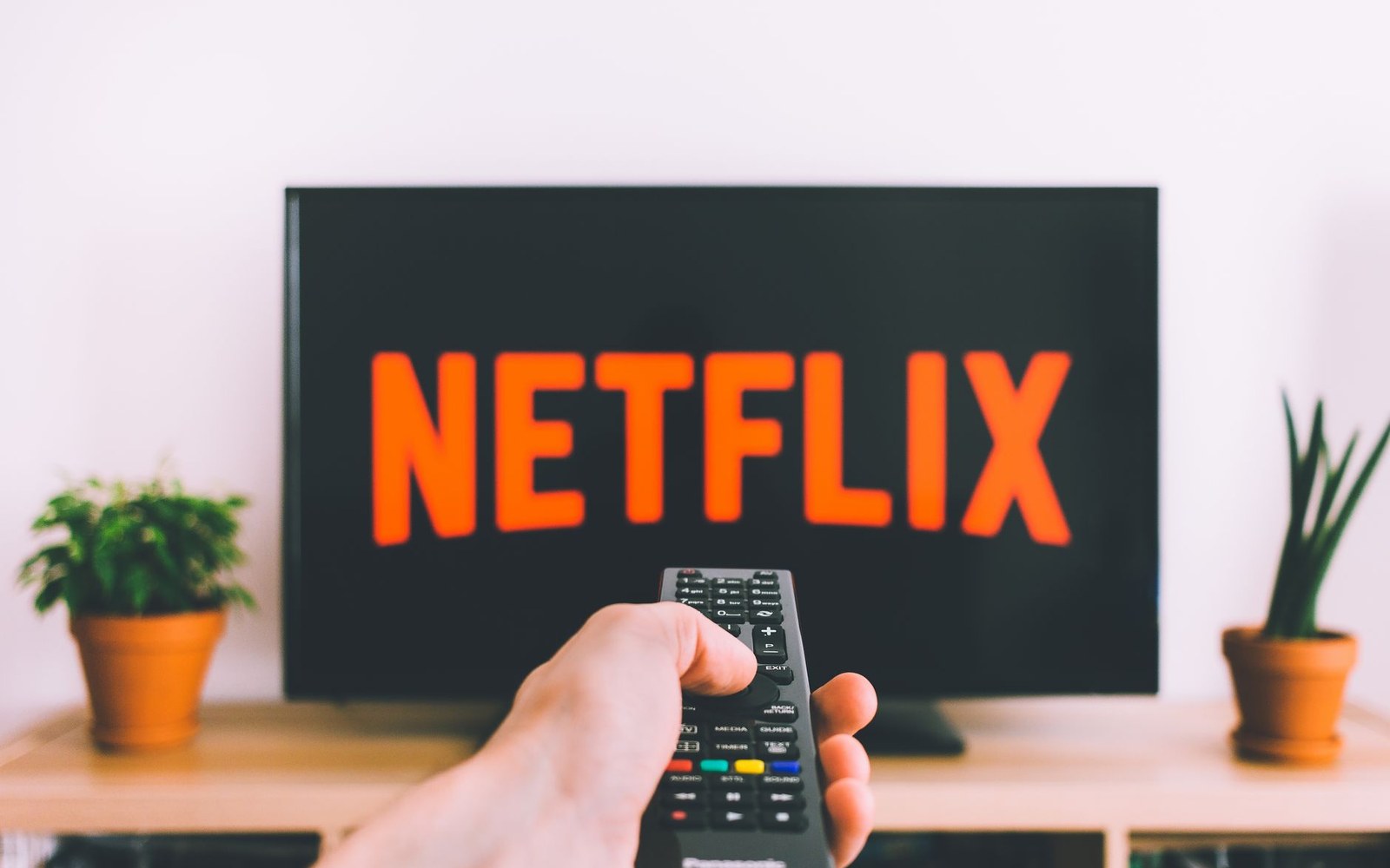 A hand points a remote at a television displaying the Netflix logo