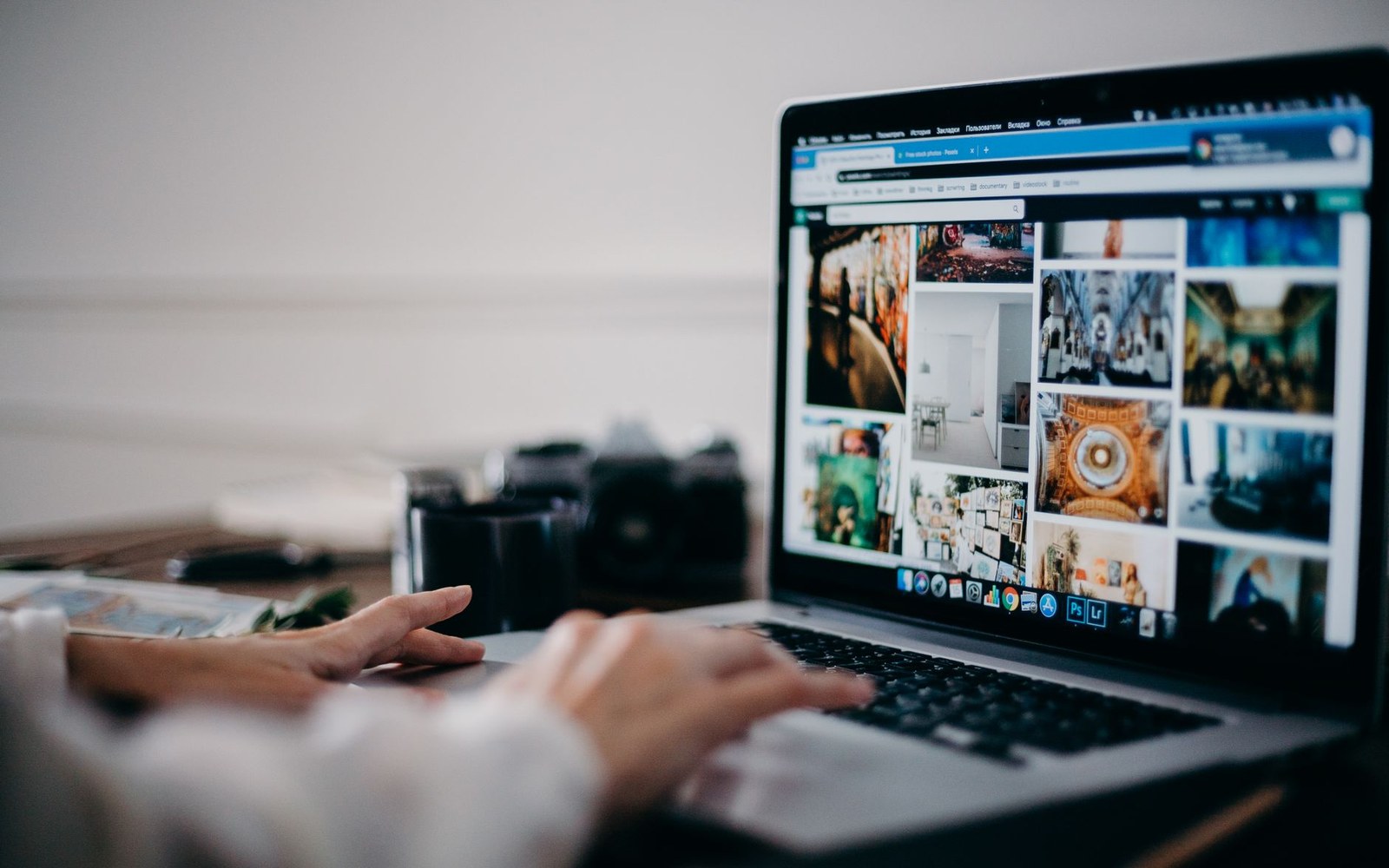 Hands typing on a laptop keyboard displaying a grid of photo thumbnails